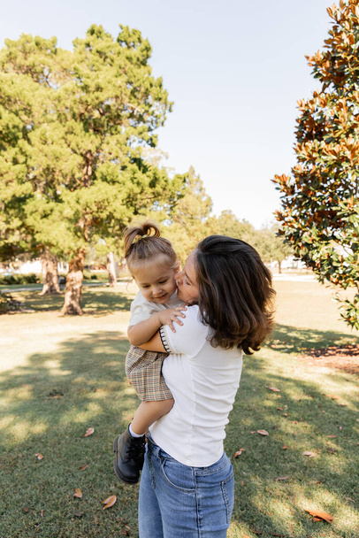 brunette mother kissing baby daughter while standing together in park of Miami  - 写真・画像
