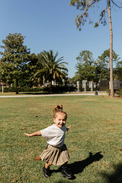 joyful toddler girl standing with outstretched hands while playing in green park  - Фото, зображення
