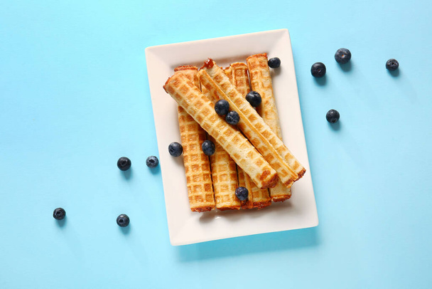 Plate of wafer rolls with boiled condensed milk and blueberries on blue background - Φωτογραφία, εικόνα