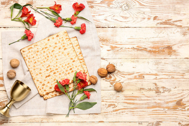 Samenstelling met Joodse platbrood matza voor Pascha, walnoten, beker en bloemen op lichte houten ondergrond - Foto, afbeelding