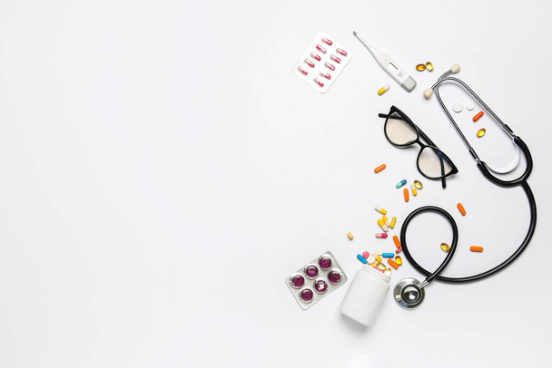 Comprimidos com óculos, estetoscópio e termômetro sobre fundo branco. Dia Mundial da Saúde - Foto, Imagem