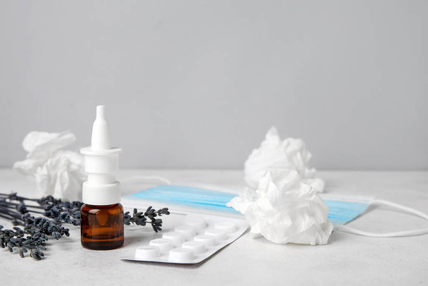 Nasal drops with pills, flowers and tissues on table near grey wall. Seasonal allergy concept - 写真・画像