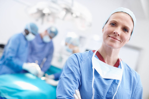 Time is life, not money in this business. Angled portrait of a mature female surgeon wearing hospital scrubs with her work colleagues in the background operating - Foto, immagini