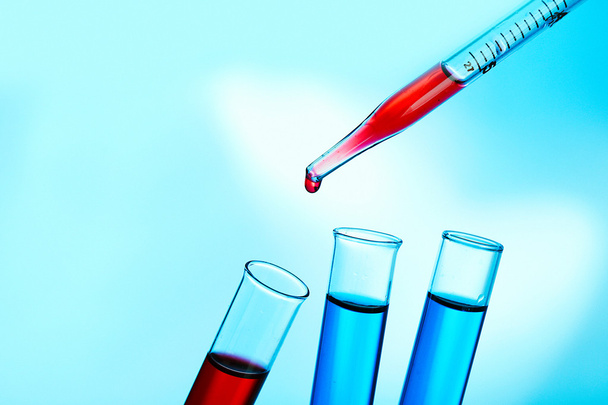 Pipette adding fluid to the one of test-tubes on blue background - Photo, Image