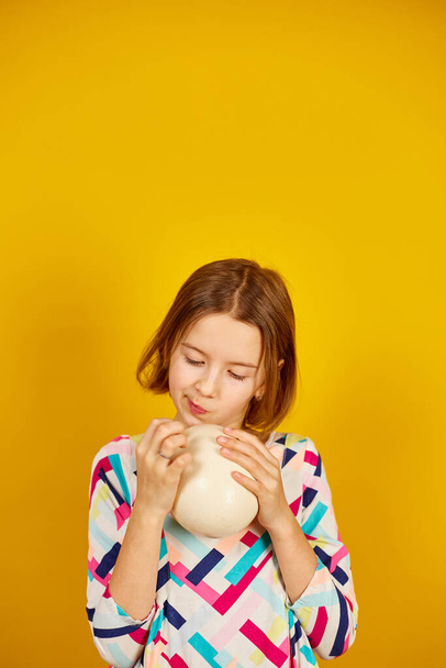 Happy playful teenager girl holding Ostrich eggs on a bright yellow studio background, celebrating Easter in style. - Foto, Imagem