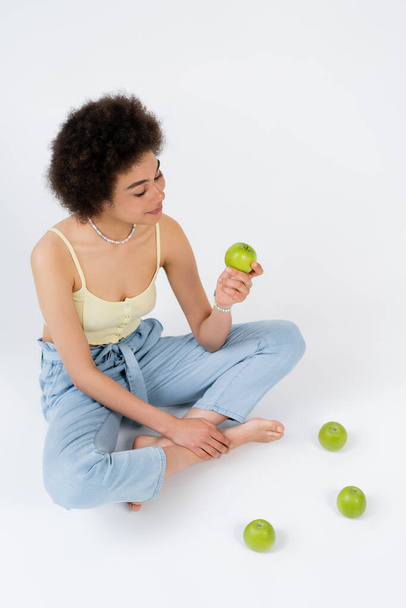 High angle view of african american woman holding apple while sitting on grey background  - Fotó, kép