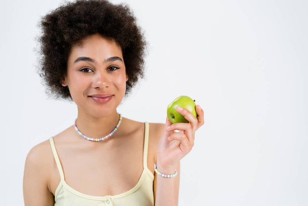 Portrait of smiling african american woman holding fresh apple isolated on grey  - Photo, Image