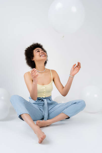 Positive african american woman throwing balloon on grey background  - Photo, Image