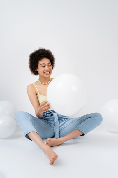 Barefoot african american woman holding balloon on grey background  - Foto, immagini