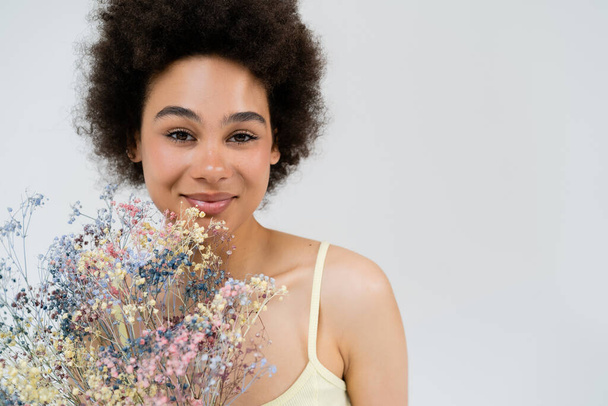 Smiling african american woman looking at camera near baby breath flowers isolated on grey  - Fotoğraf, Görsel