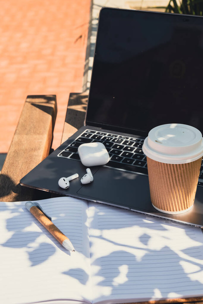 Kaffee zum Mitnehmen in Bastel-Recycling-Pappbecher mit Papier-Notebook-Laptop mit drahtlosen Kopfhörern. Mockup Kaffeepause. Audio-Heilung, Klangtherapie Wellness-Rituale, positive psychische Gesundheitsgewohnheiten - Foto, Bild