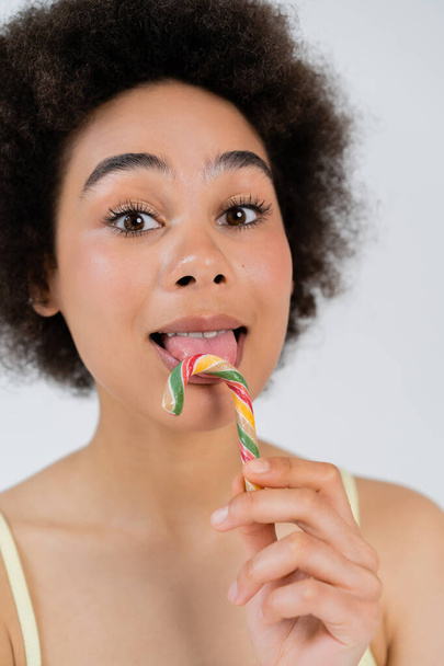 Afro-Amerikaanse vrouw likken candy cane geïsoleerd op grijs  - Foto, afbeelding