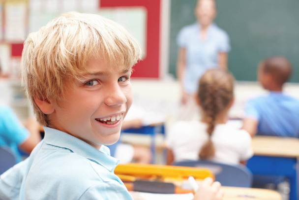 He loves school. Portrait of a cute blonde boy in sitting at a desk in class - Фото, изображение