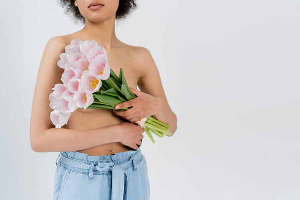 Cropped view of young african american woman with naked shoulders holding flowers isolated on grey  - 写真・画像