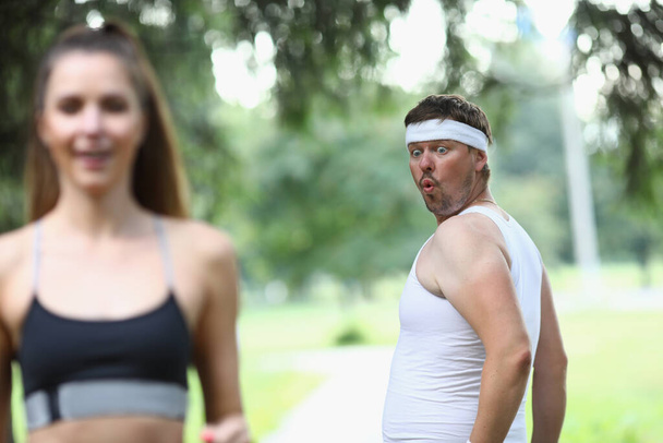 Чоловік ревнує до красивої бігової жінки і дивиться на дупу в парку. Фітнес і спортивна концепція
 - Фото, зображення