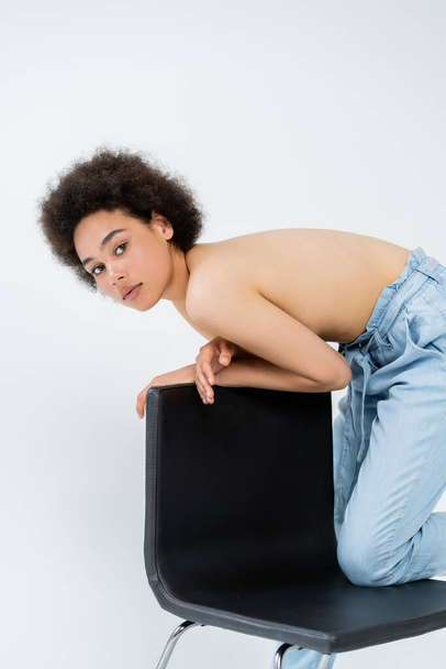 Shirtless african american woman in pants posing near chair isolated on grey  - Photo, Image