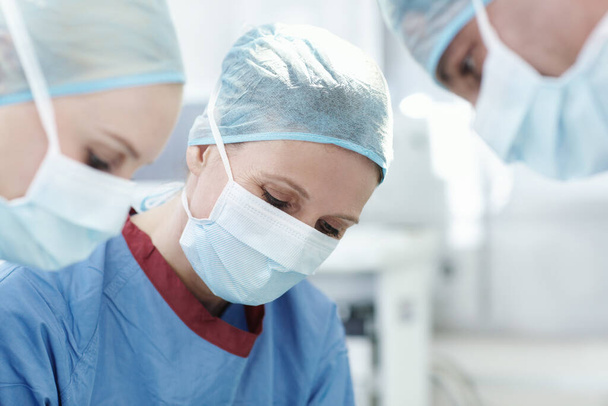 Sakin ve odaklanmış bir tıbbi uzman. Ameliyatta meslektaşlarıyla birlikte çalışan bir kadın cerrahın yakın çekimi. - Fotoğraf, Görsel