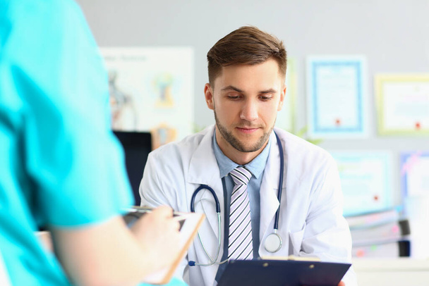 Male doctor carefully examines documents in office of clinic at workplace. Medical diagnosis and treatment prescription concept - Photo, image