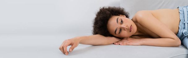 Bez košile africký americký model ležící na gauči na šedém pozadí, prapor  - Fotografie, Obrázek