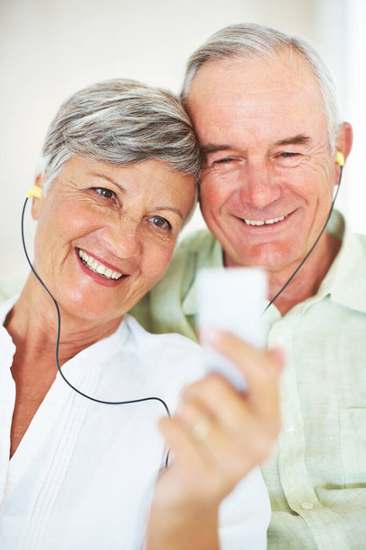 Lächelndes älteres Paar, das zusammen Musik hört. Nahaufnahme eines lächelnden reifen Paares, das zu Hause gemeinsam Musik hört - Foto, Bild