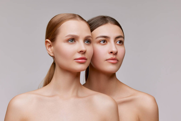 Confidence. Couple of beautiful elegant young women, blond and brunette with well-kept skin posing over light background. Concept of natural beauty, fashion, skin care and health, ad - Photo, Image