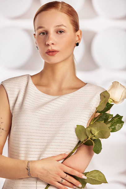 Kolsuz doğmuş, güzel, engelli bir kadının portresi. Beyaz bir elbisenin içinde elinde bir çiçek tutuyor. Çeşitlilik engeli ve çiçekler - Fotoğraf, Görsel