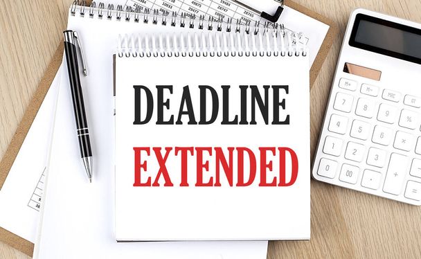 DEADLINE EXTENDED is written in white notepad near a calculator, clipboard and pen. Business - Foto, afbeelding