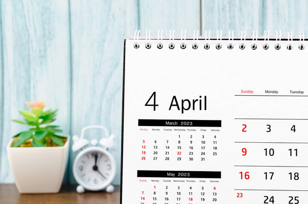 April 2023 Monthly desk calendar for 2023 year with alarm clock on blue wooden background. - Foto, Imagem