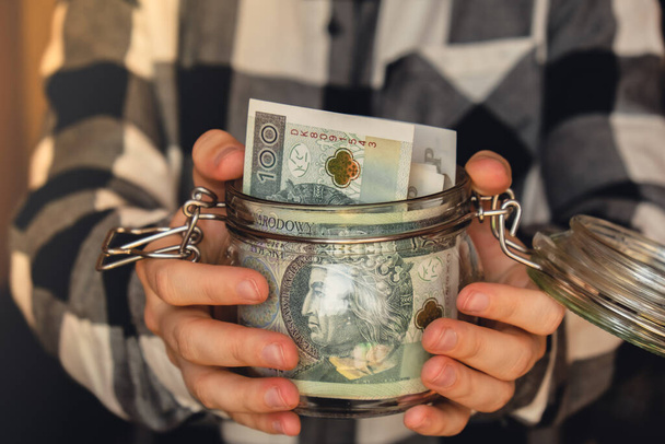 Polish zloty banknote saving money in glass jar. Unrecognizable woman moderate consumption and economy Collecting money. Tips. Business, finance, saving, banking and people concept. Extra money - Φωτογραφία, εικόνα