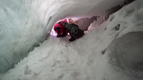 厚い氷河の下の氷の洞窟に登山リュックを持つ男。ようこそ白い雪は、巨大な石が表示され、氷の鍾乳石がハングします。気泡が凍結した透明な氷。いいですね - 映像、動画
