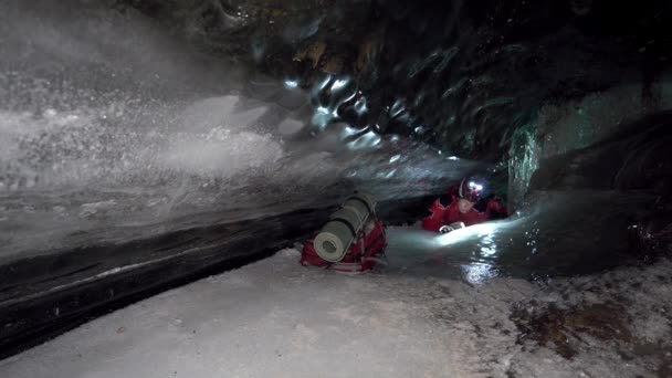 リュックを持った男が氷の洞窟の周りを移動します。濃い青の色の美しい氷の壁のシマー。場所には大きな石があります。雪の天井。山の中の氷河の中を歩くのは難しい - 映像、動画