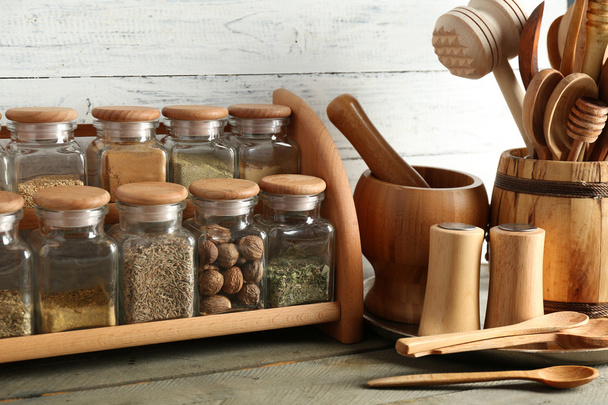 Different spices in glass bottles on stand with utensils on wooden table and planks background - Foto, afbeelding
