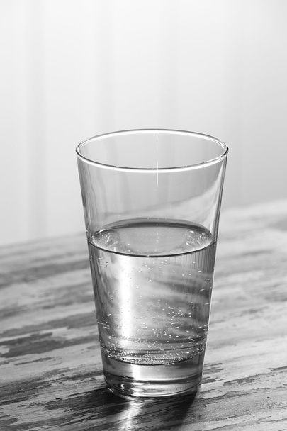 Glass of clean mineral water on old color wooden surface and planks background - Photo, image