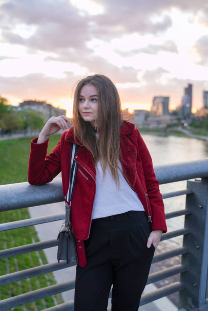 Prachtig Litouws meisje staat op de Mindaugasbrug in het centrum van Vilnius, hoofdstad van Litouwen. Ik draag een rode jas. Terugkijkend. Zonsondergang Licht - Foto, afbeelding