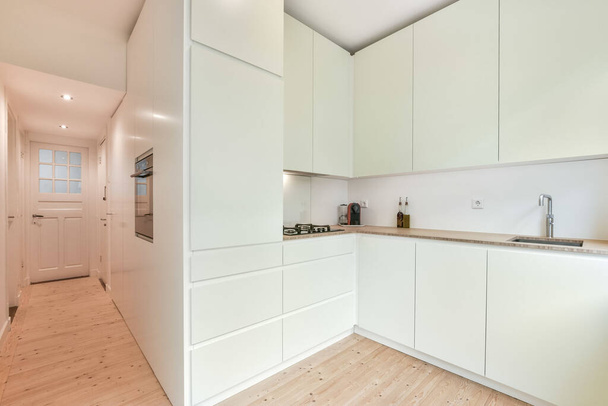 a kitchen with white cupboards and wood flooring in an apartment, taken from the side view looking towards the dining area - Valokuva, kuva