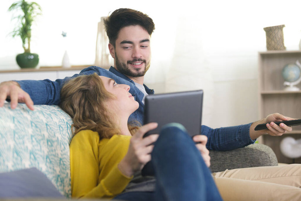 couple relaxing on sofa using tablet and watching tv - Foto, imagen