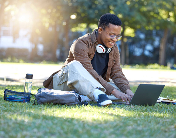 Black man, park studying and laptop work in a campus garden with a smile and lens flare, Outdoor, happiness and online elearning with a textbook of a student busy with exam study on university grass. - Foto, immagini