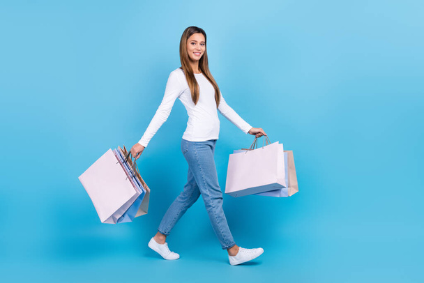 Full length photo of sweet charming lady dressed white shirt holding bargains empty space isolated blue color background. - 写真・画像