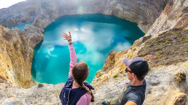 Couple standing at the volcano rim and watching the Kelimutu volcanic crater lakes in Moni, Flores, Indonesia. They are having fun, enjoying the view on lake shining with many shades of turquoise - Foto, imagen