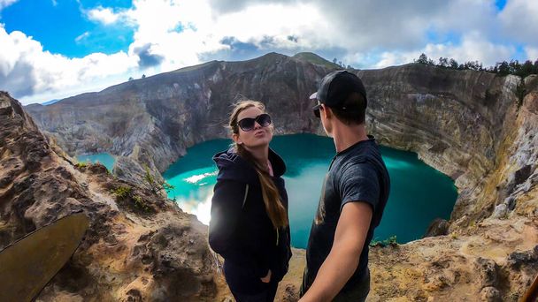 Couple standing at the volcano rim and watching the Kelimutu volcanic crater lakes in Moni, Flores, Indonesia. They are having fun, enjoying the view on lake shining with many shades of turquoise - Foto, Imagen