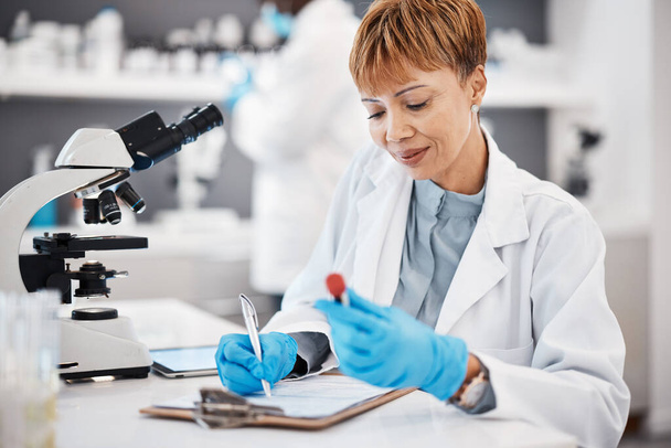 Scientist, woman and writing report with results, focus or analytics in pharma laboratory. Science expert, checklist or research with blood sample, medical innovation or study at pharmaceutical trial. - Photo, Image
