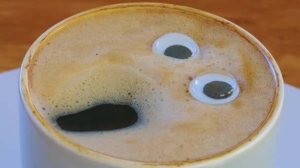 Glimlachende koffieman in een kopje. Geurende, levendige koffie met ogen en mond. Menselijk gezicht op verse, melkachtige koffiemelk. Hoge kwaliteit 4k beeldmateriaal - Video