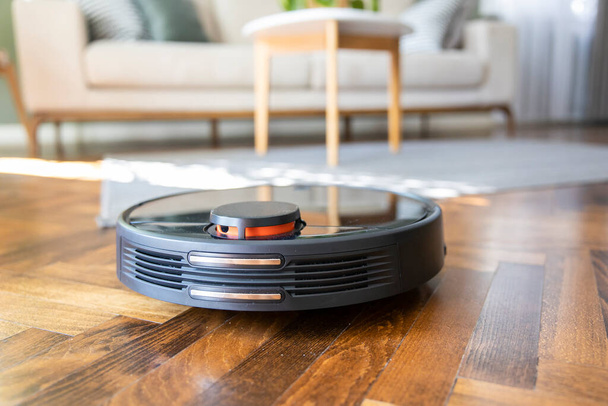 Robot vacuum cleaner on the parquet floor. Cleaning in living room at home - Foto, Bild