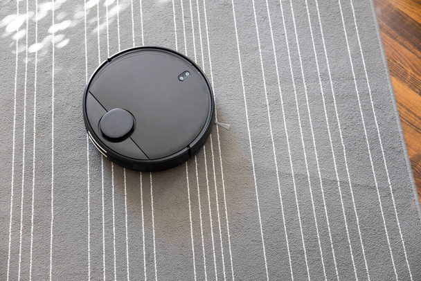 Robot vacuum cleaner on the carpet. Cleaning in living room at home - Foto, Imagem