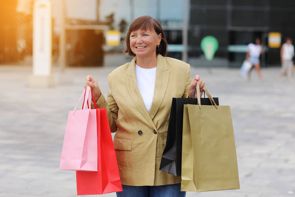 Seasonal Sales. Happy adult woman with shopping bags. Middle ages female after shopping on shopping mall background. Purchases, discounts, sale concept. Online shopping concept, Black friday. mockup. - Foto, Bild