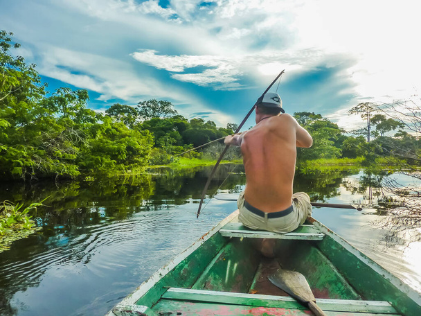 Un joven arquea la caza de Pirañas, en medio de la selva amazónica en Brasil, desde un pequeño barco local. - Foto, Imagen