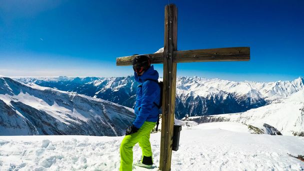 Skier supporting on a cross, admiring the Alpine view from Heiligenblut am Grossglockner and Innerkrems. Endless chains of mountains. Skier wears a helmet and googles. Lots of fresh powder snow. - Foto, imagen
