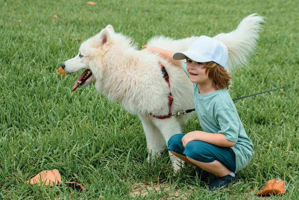 Little boyhugging white fluffy samoyed dog and laughing in the park or spirng grass background - Foto, Imagen