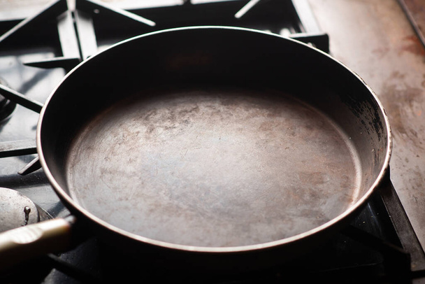 Empty pan on the stove. An old frying pan is heated in a home kitchen. - Фото, зображення