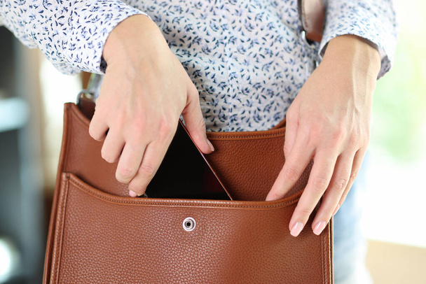 Close-up of woman putting smartphone in brown leather crossbody. Female take out cellphone of stylish bag - Fotoğraf, Görsel